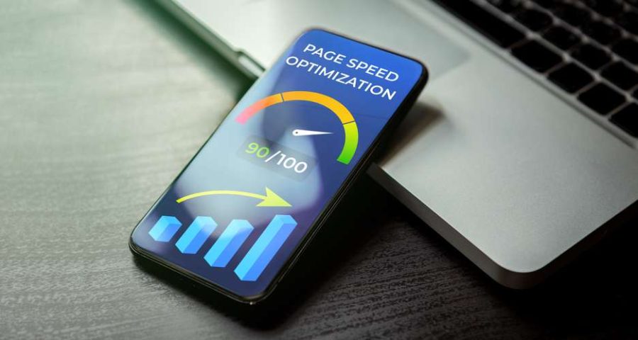 A close up of a smartphone leaning up against a laptop bottom. On the screen reads "page speed optimization" and shows a speedometer with different colors at each end to represent speed levels.