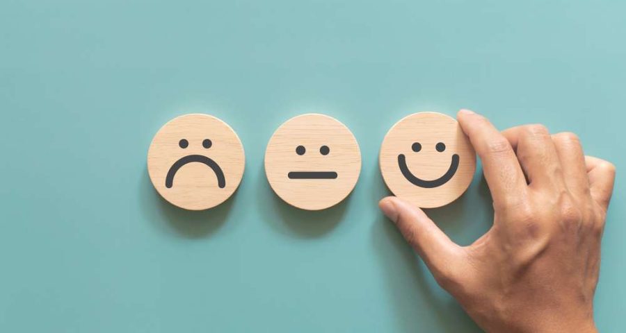 A person placing three wood blocks with a frown face, neutral face, and smiley face
