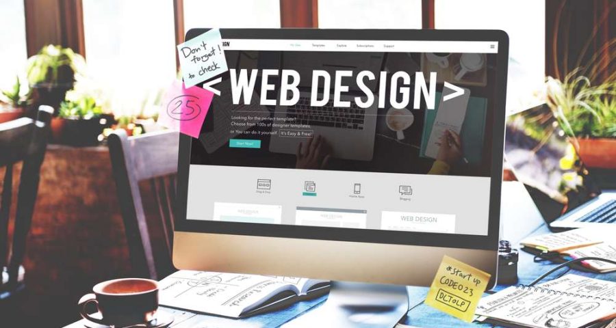 A desk cluttered with papers with a desktop monitor at the center. The monitor showcases a web page with "Web Design" written in big letters across the top