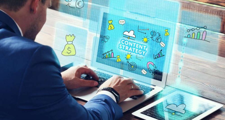 A man types at his laptop next to a tablet. The screen reads "content strategy", which is a big part of SEO and topical authority.